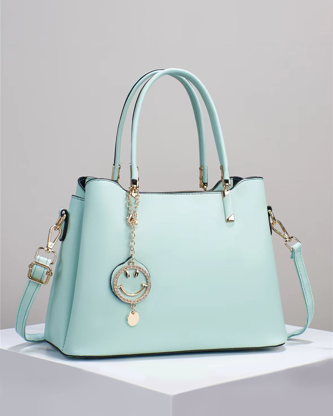 Bolso de mano con colgante sonriente. Detalles en dorado. Tiro para hombro