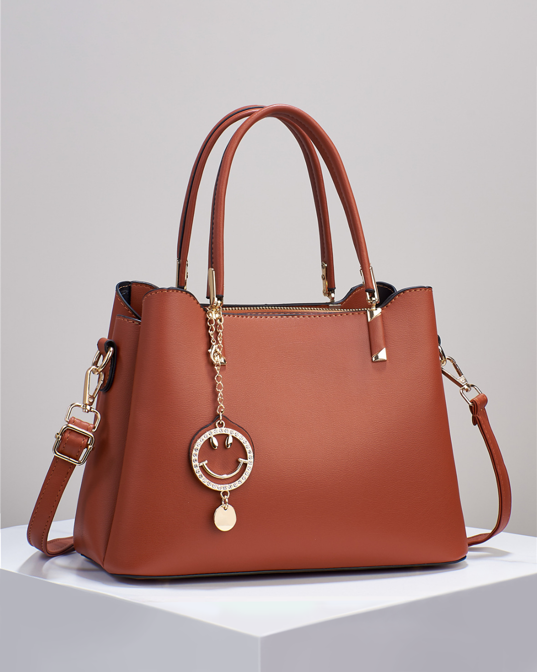 Bolso de mano con colgante sonriente. Detalles en dorado. Tiro para hombro